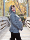 Pregnant woman in hooded gray maternity sweater standing on a bridge.