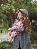 Woman holding a baby and wearing a hooded gray nursing sweater with pockets. 